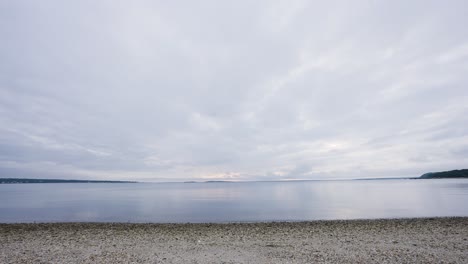 Calm-water-in-Noyack-Bay-NY-near-Sag-Harbor,-just-before-sunset,-the-beach-is-very-rocky,-land-can-be-seen-in-the-distance