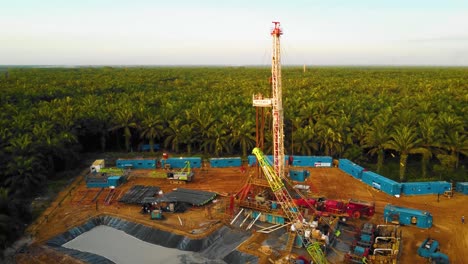 cinematic 4k drone footage of onshore drilling rig equipment structure for oil exploration and exploitation in the middle of jungle surrounded by palm oil trees during sunset and high oil price