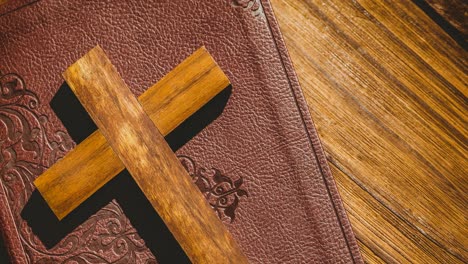 wooden christian cross on bible in leather cover over wooden surface