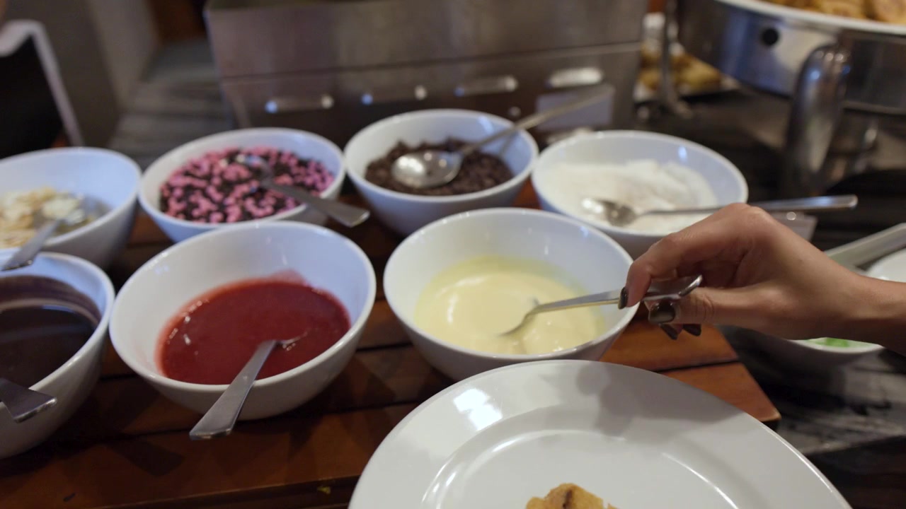 Una persona versa a filo salsa al cioccolato bianco sulla torta con un cucchiaio a un buffet di ristorante.