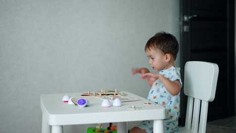 small kid looks at puzzles on the table in front of him. lovely baby boy waves his hands excitedly.