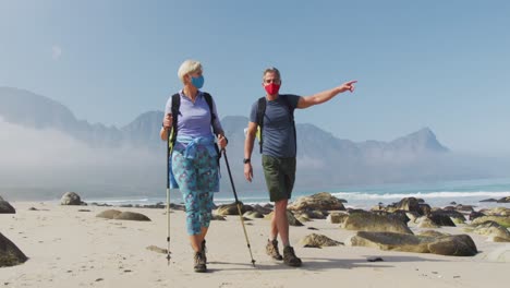 senior hiker couple wearing face masks with backpacks and hiking poles pointing towards a direction