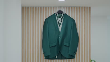 green formal jacket and shirt hung on a wooden hanger indoors
