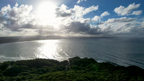 sunlight beams through clouds over byron bay's lush coastline, waves sparkle in the distance