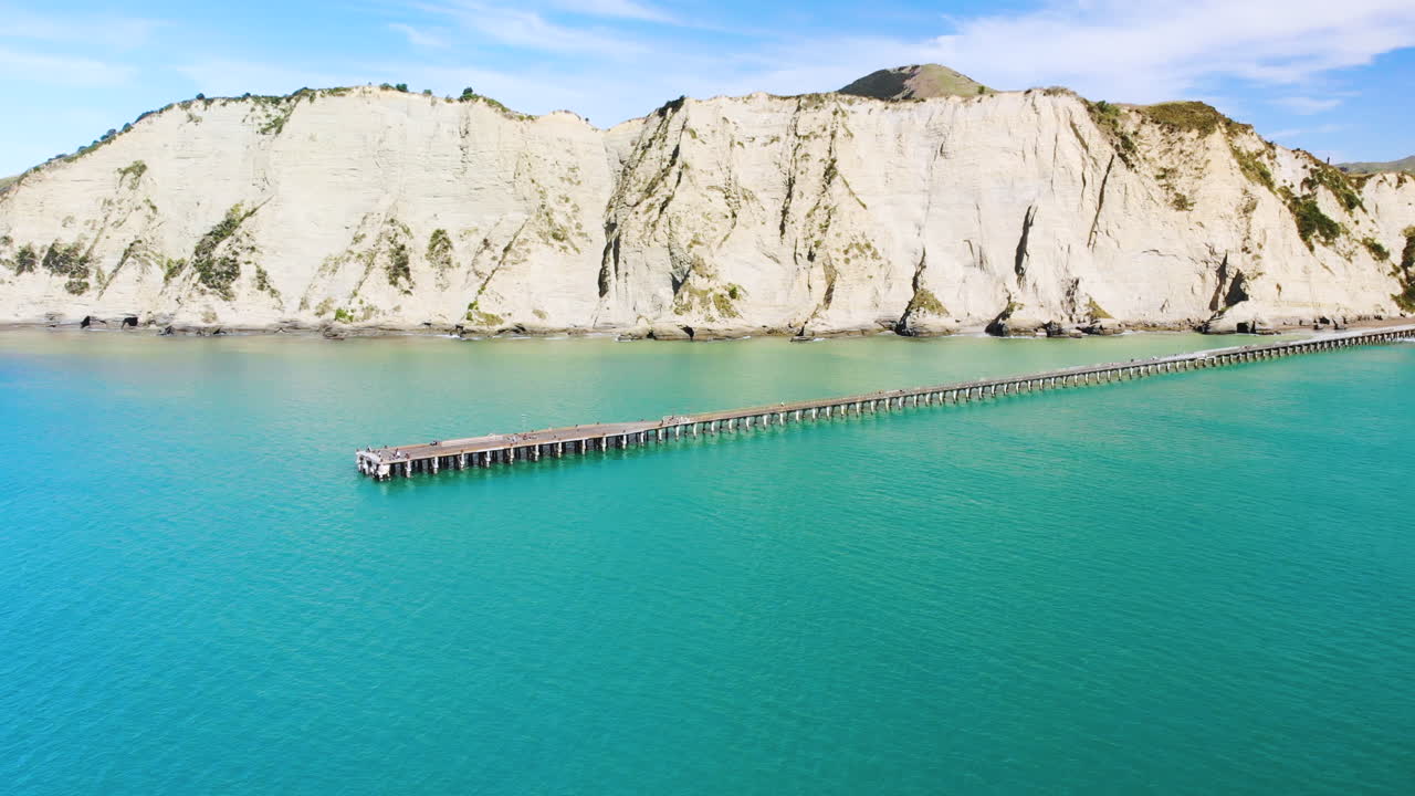 뉴질랜드 톨라가 만 에 있는 푸른 바다 에 있는 톨라가 만 항구 와 그 배경 에 있는 거친 산악 절벽
