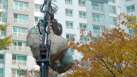 Bolsas-De-Basura-Levantadas-Y-Transportadas-Sobre-Un-árbol-Amarillo-De-Otoño-Por-Un-Camión-De-Basura-Operado-Por-Un-Hombre-Con-Brazo-De-Garra