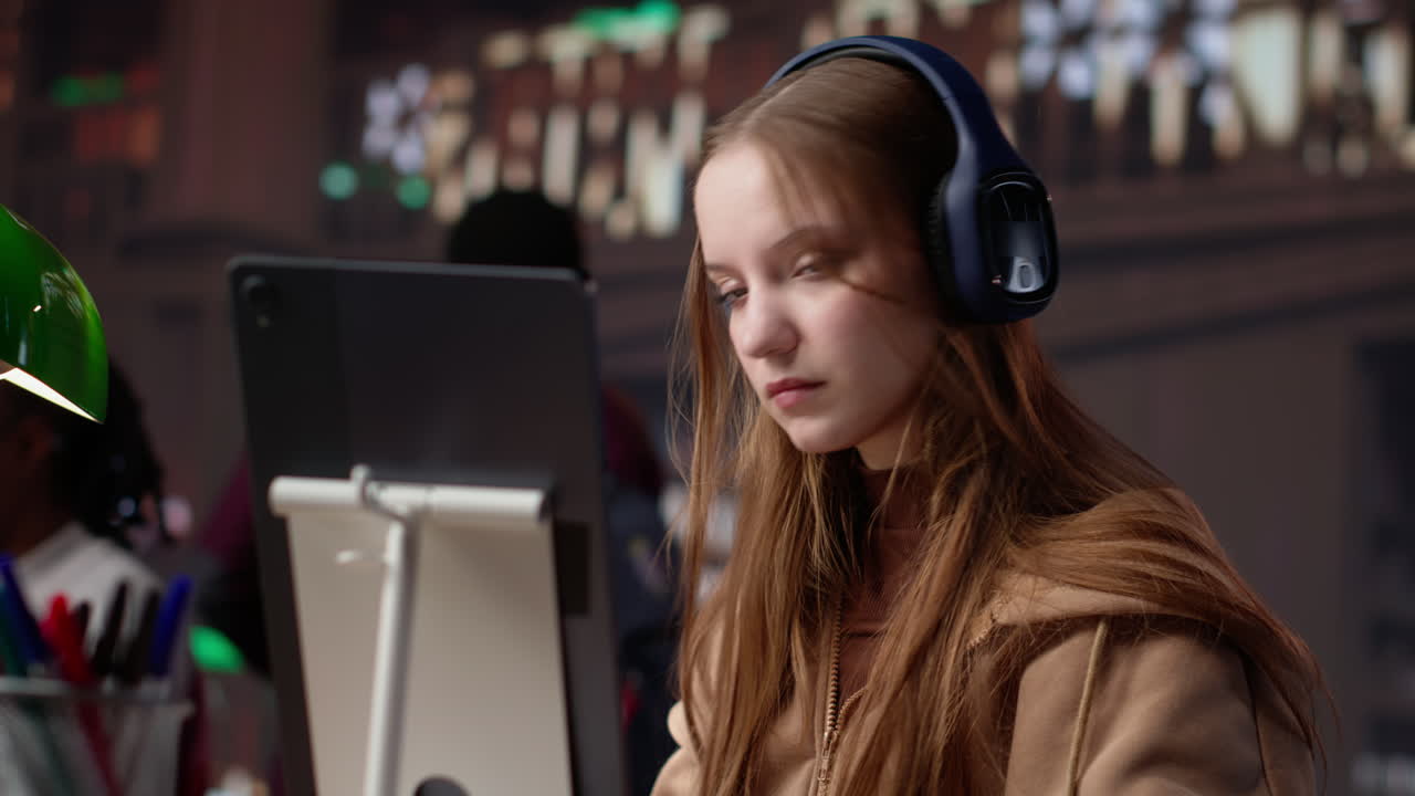 Vertical video young girl listening to educational documentary on laptop and taking notes