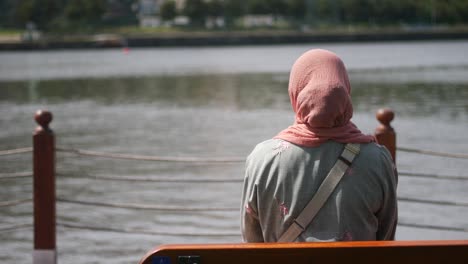 una mujer en hijab sentada en un banco mirando el lago