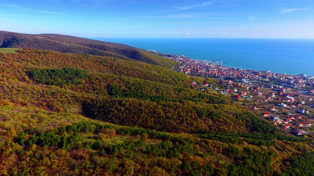 Bulgaristan'da sahil kasabası yakınında ormanlık vadi. Kırmızı çatılı binalara ve denize doğru inen bir yamaçta sonbahar ve yaprak dökmeyen ağaçların drone görüntüsü.