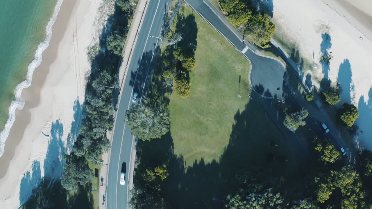 Aerial view of beachside road passing through tropical greenery in Vung Tau, Vietnam. The smooth road curves along the coast with a lush green landscape on one side and sandy beach on the other