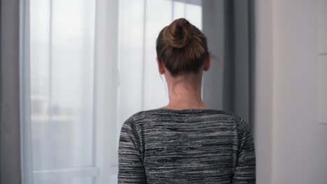 Back-View-Of-Young-Woman-Opening-Her-Bedroom-Curtains-And-The-Window-And-Looking-Outside-In-Slowmotion