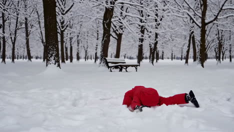 child in red snowsuit playing and crawling in a snowy park