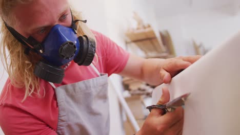 caucasian male surfboard maker wearing a face mask and making a surfboard