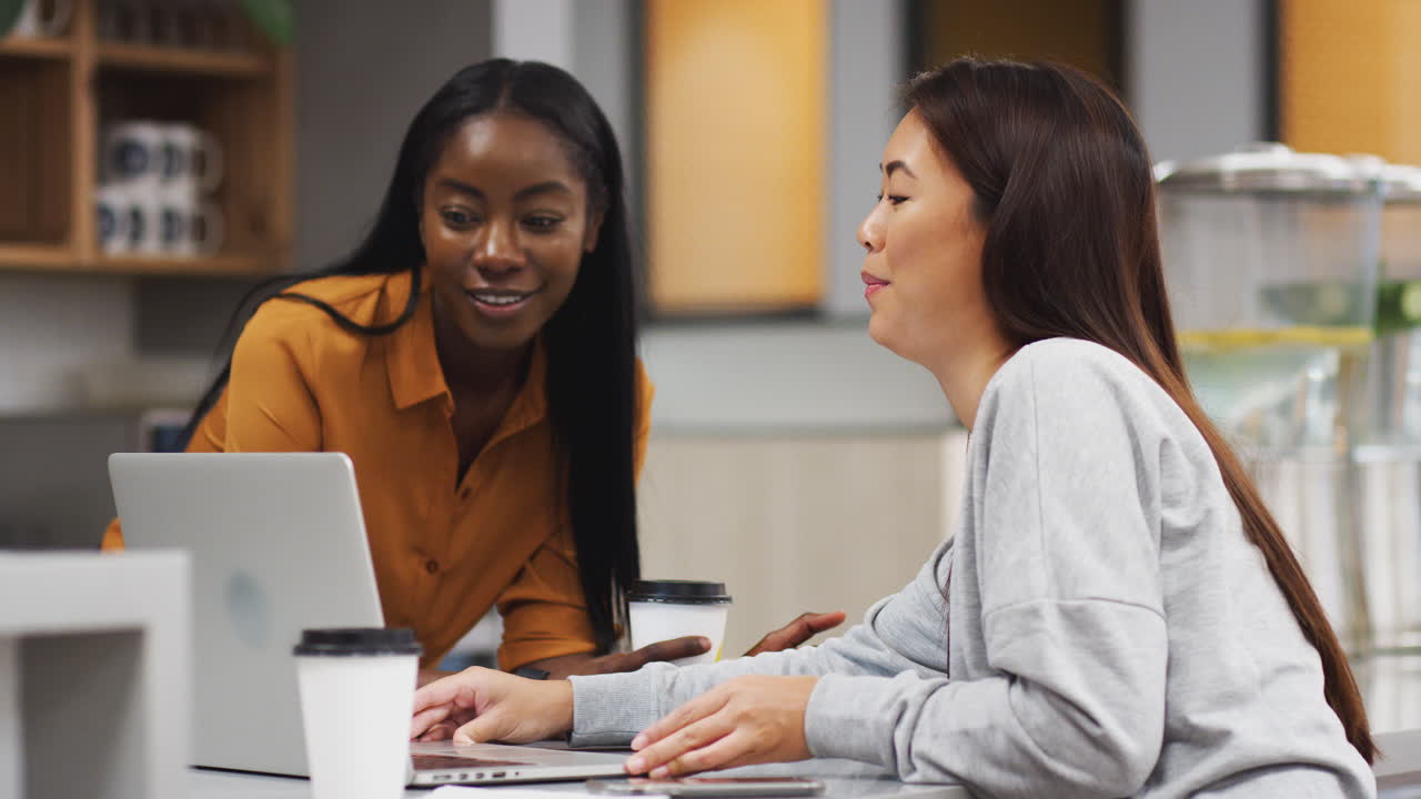 dos mujeres de negocios trabajando en una computadora portátil en el área de la cocina de una oficina moderna