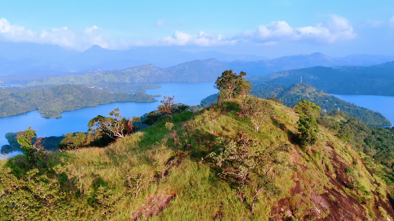 Flight around the mountain top overgrown with grass and some trees. Azure waterscapes surrounded by picturesque rocks at backdrop. Aerial view.