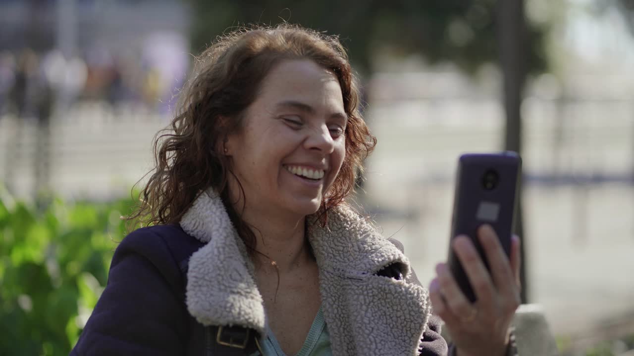 Smiling curly woman waving and talking to friend during video call