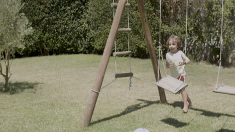 front view of happy kid in t-shirt and shorts running in the garden, kicking ball and looking at camera