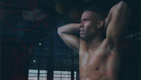 in gym, shirtless man with arms behind head looking determined