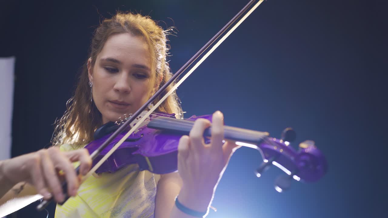 violínista joven tocando el violín en una habitación oscura. fondo negro.