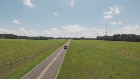 Aerial-shot-of-red-pickup-truck-traveling-a-down-country-road-on-a-summer-day