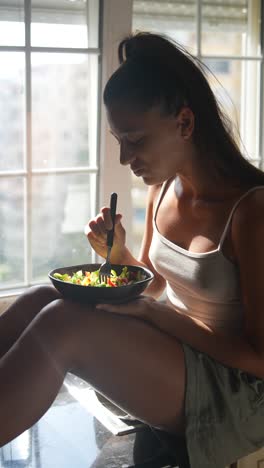 young woman eating salad by the window