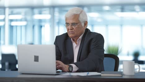 serious senior indian manager working on laptop