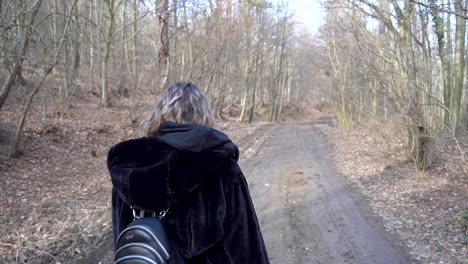 mujer joven caminando por el bosque con una chaqueta negra en otoño