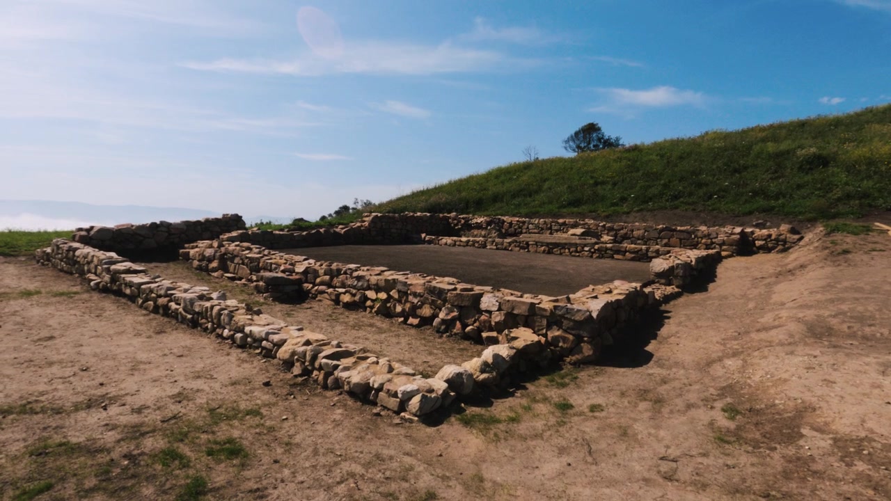 Fondamenta in pietra romane presso il sito archeologico di La Campa Torres, Gijón. Collina verde sotto un cielo blu