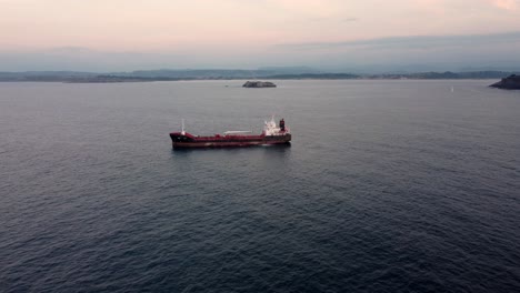 industrial tanker vessel near coastline of spain with remote island lighthouse, aerial view