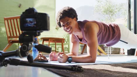 Happy fit african american man exercising at home, doing press ups and filming fitness vlog
