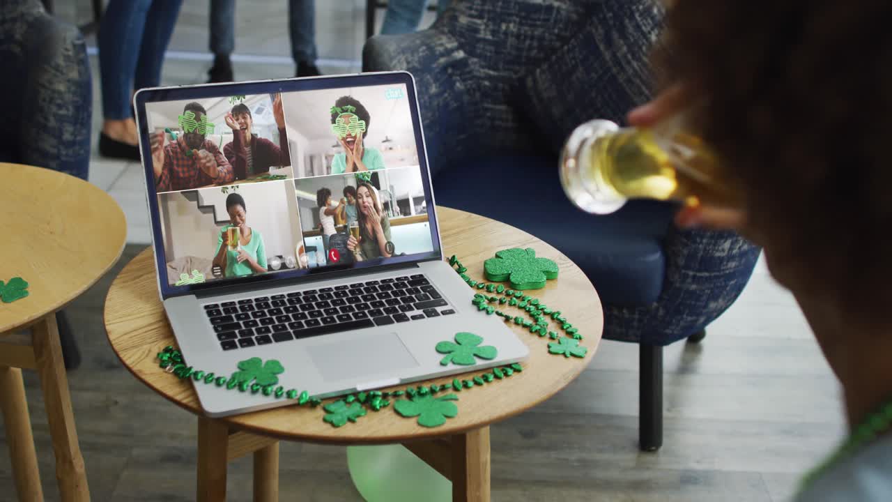 Smiling diverse group of friends with beer wearing clover shape items on video call on laptop