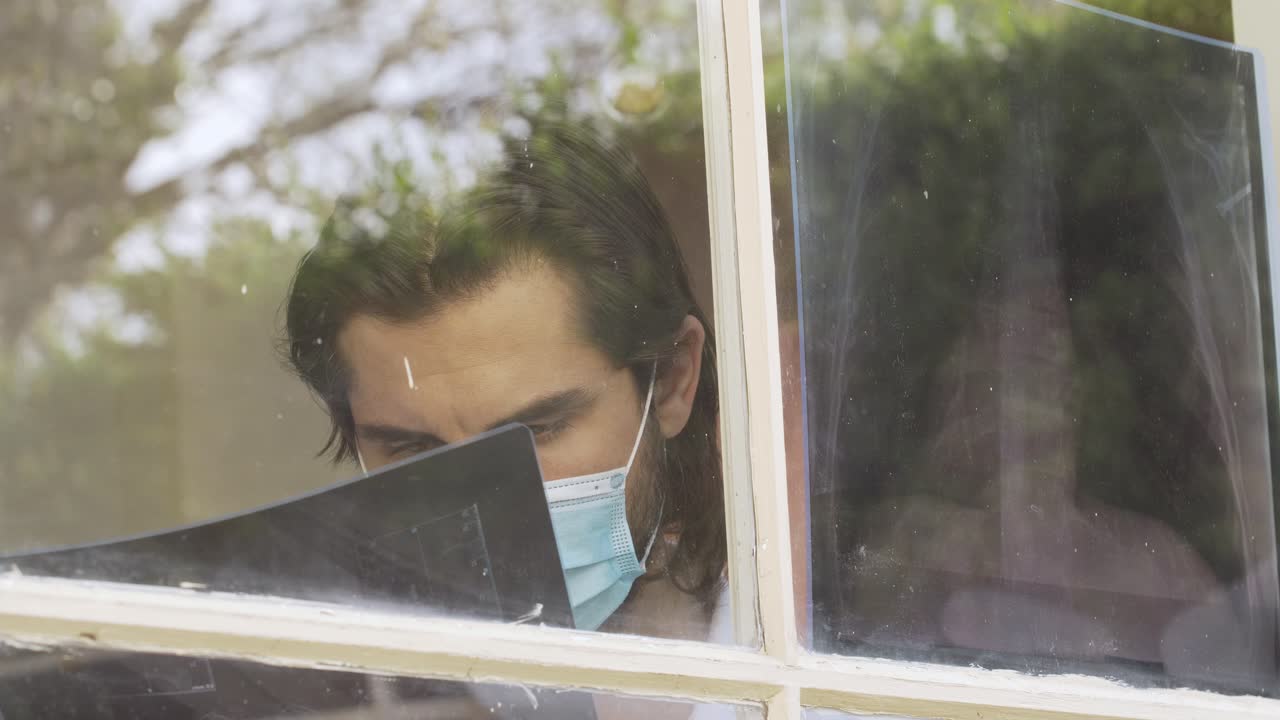 doctor with surgical mask looking at an X-ray film behind glassy window