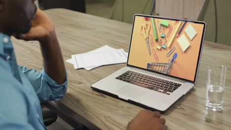 African-american-man-at-table-using-laptop,-online-shopping-for-staionery,-slow-motion