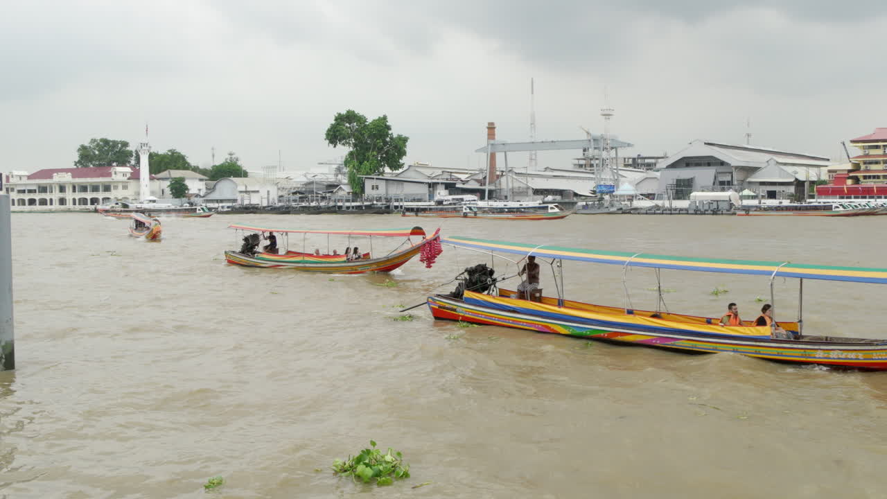 Tourists taking a ride on long wooden boats while cruising along the Chao Phraya River in Bangkok, Thailand.
