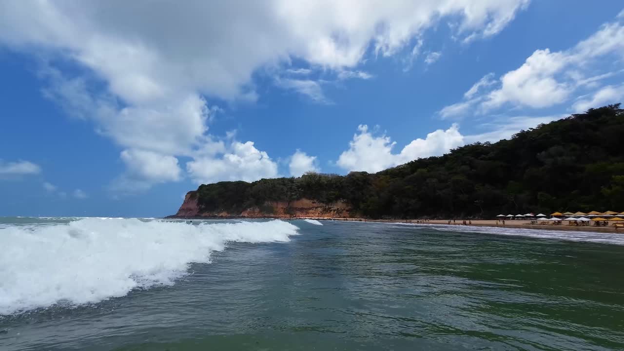 toma de mano de pequeñas olas que chocan contra la cámara desde la playa tropical de madeiro en pipa, brasil, en el estado de río grande do norte, con aguas cálidas y claras de color turquesa rodeadas de grandes acantilados