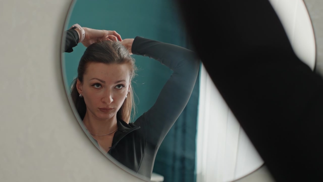 Donna che si prepara per l'esercizio mattutino. Una donna si sistema i capelli prima di iniziare una sessione di allenamento. Una donna energica si sistema i capelli davanti allo specchio prima di fare esercizio al mattino.