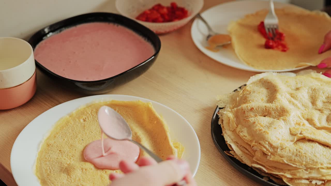 Romantic teamwork as couple prepares crepes with fruit cream on wooden table