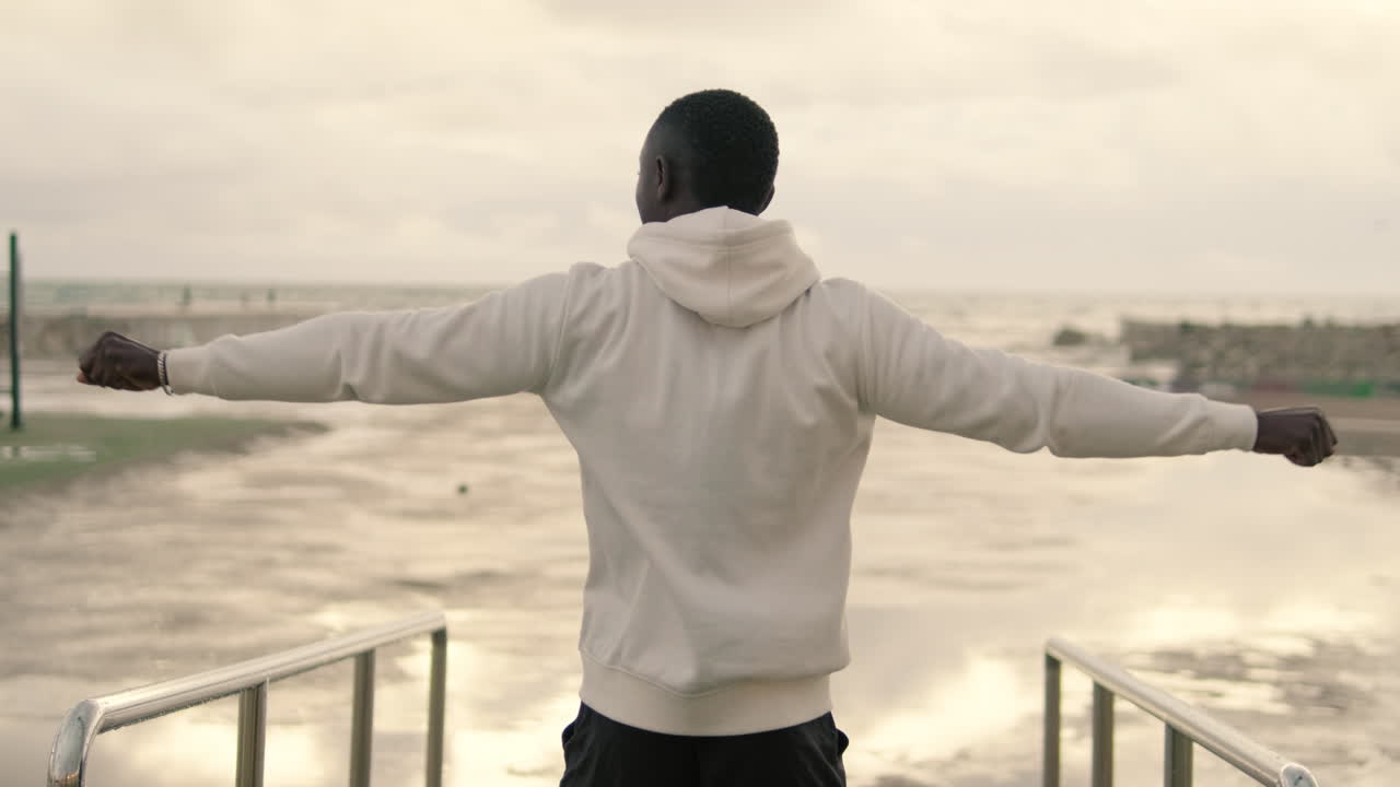 Young Black Man Standing with Arms Outstretched on Wet Ground