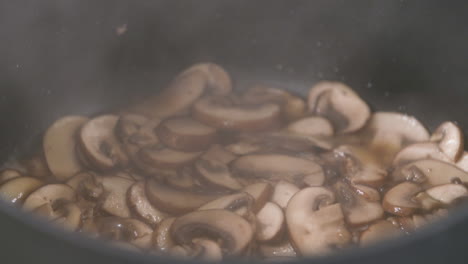 close up of cooking hot steaming brown mushrooms in a pan