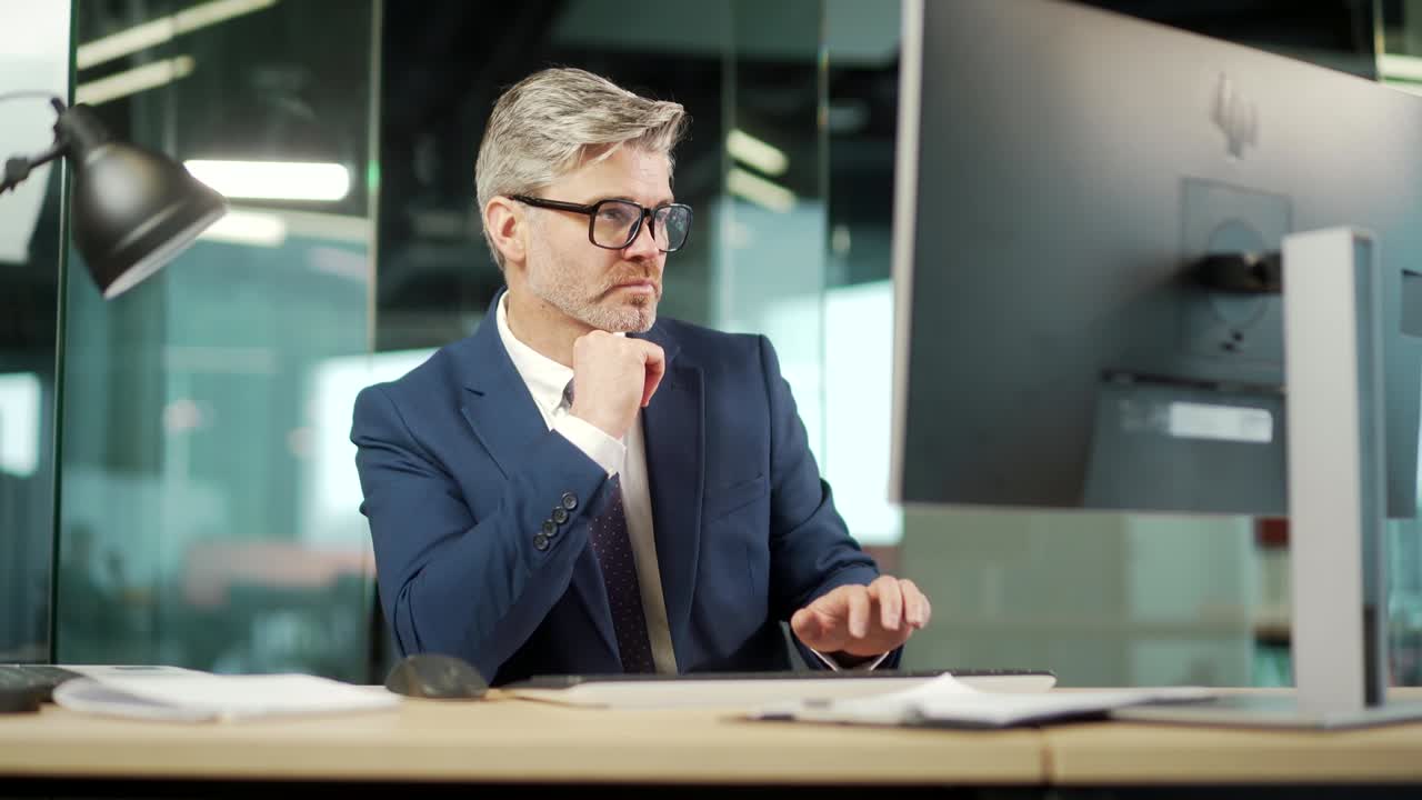 Portrait thoughtful male businessman working on pc computer at a modern office desk. Confident Focused pensive business man employee in suit indoor