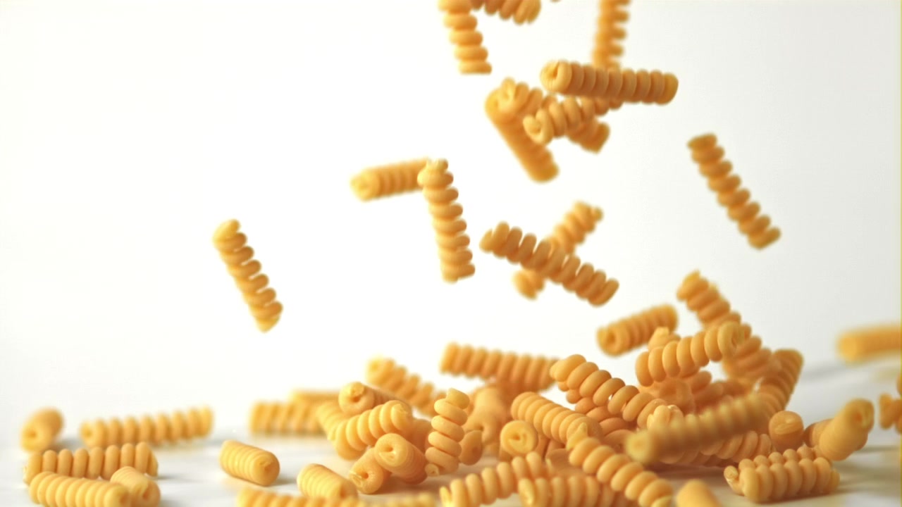 Raw Fusilli Pasta Falling onto a White Surface