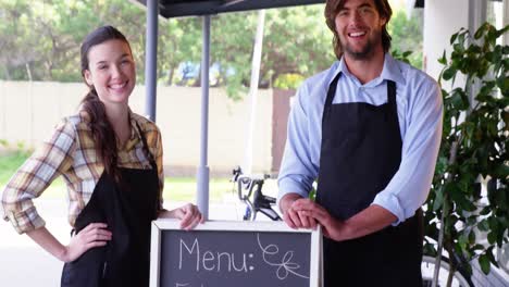 waiter and waitress standing with menu board outside the cafe