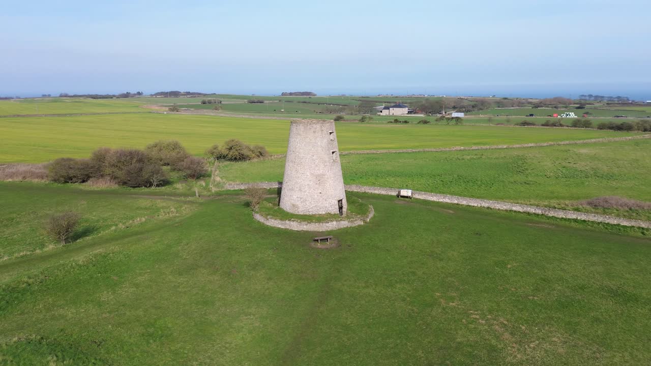 Cleadon Yel Değirmeni'nin Kuzey Denizi yakınlarındaki açık yeşil tarlalar üzerinde dronla yörünge uçuşu, Cleadon, South Tyneside, İngiltere. Kırsal kesimde açık bir günde tarihi taş kule simgesi.