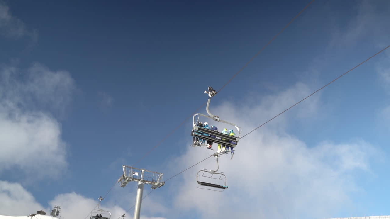 푸른 하늘과 푹신한 구름이 있는 완전히 점유된 스키 의자 리프트 장치 횡단 프레임