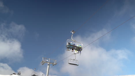 fully occupied ski chair lift unit crossing frame with blue sky and fluffy clouds