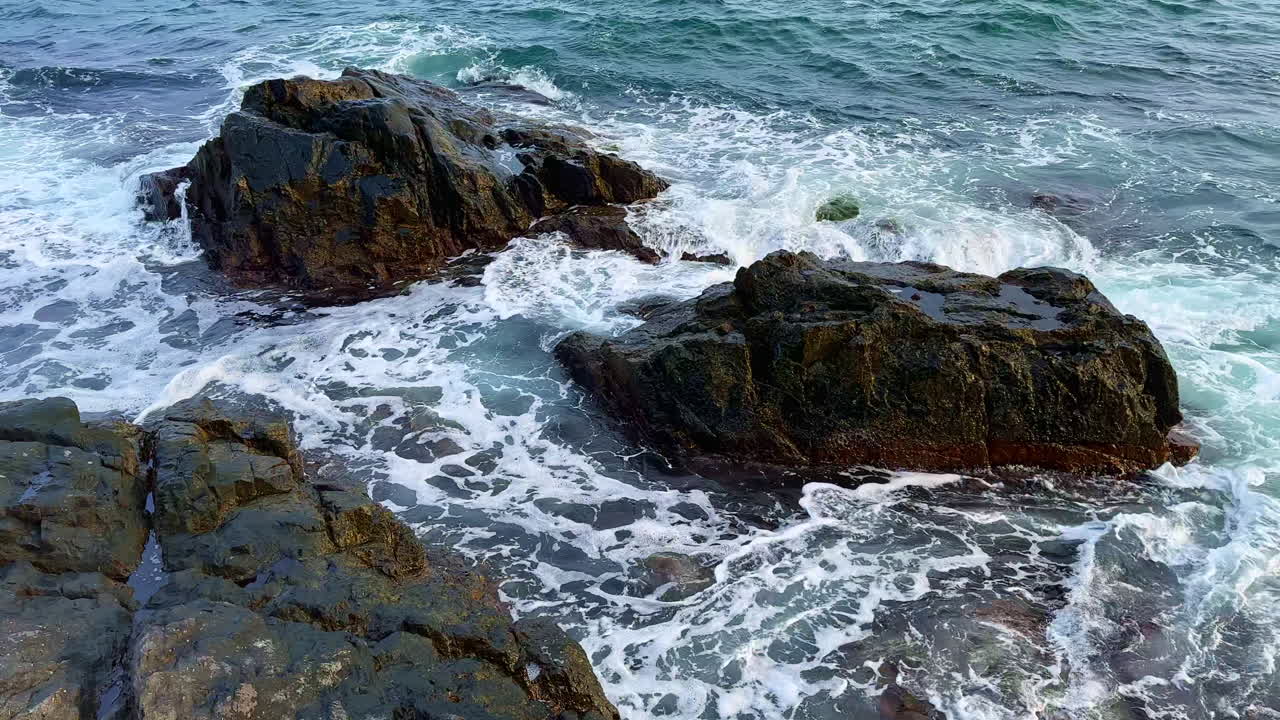 Bølger slår mot steiner ved strandlinjen i et kystområde på dagtid