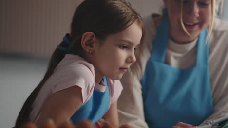 una encantadora niña y su madre están leyendo un viejo libro de cocina en la cocina de casa aprendiendo a cocinar