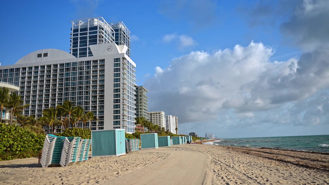 Condominios de gran altura frente a la playa a lo largo de la costa de Miami Beach. Edificio de gran altura frente a la playa con palmeras, cabañas, sendero de arena, océano, nubes, Miami Beach.