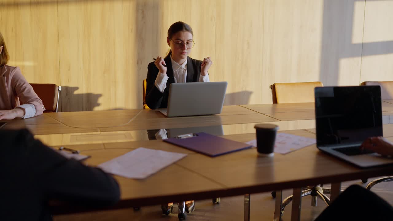 A tired girl in round glasses and a business uniform a businesswoman, sits at the table and tries to relax during a hard day at work with her colleagues