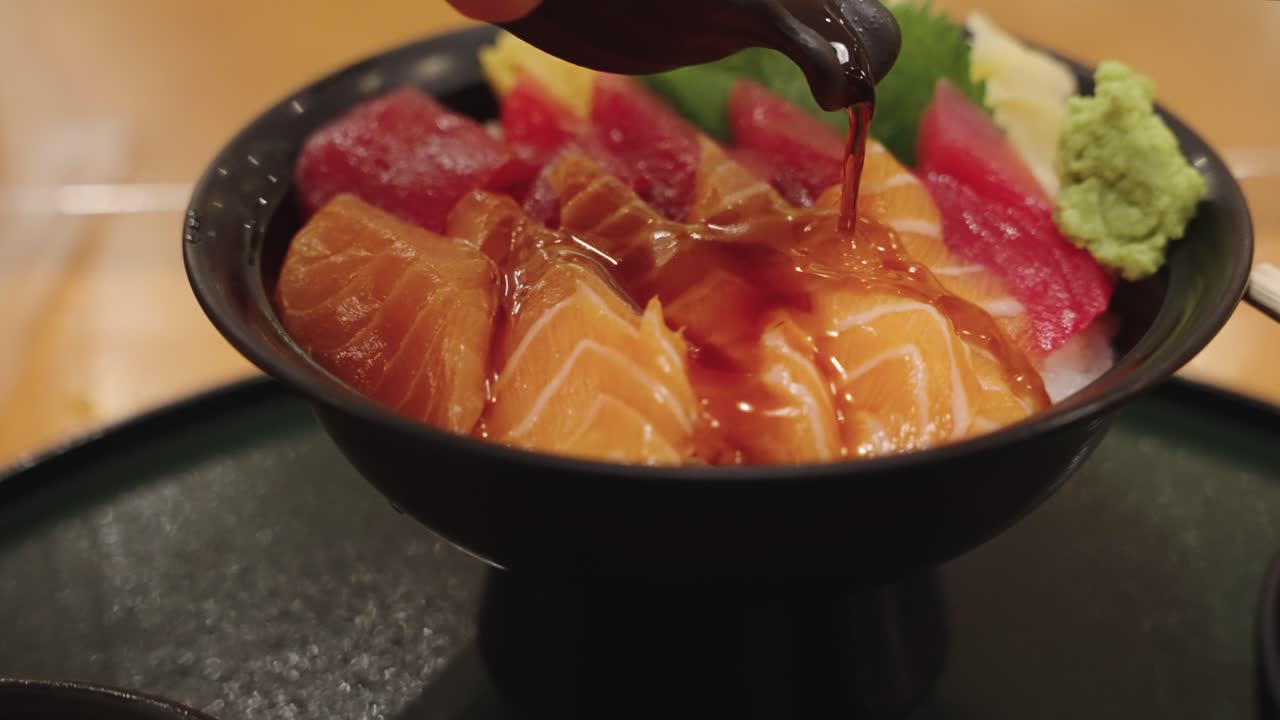 tazón de arroz sashimi japonés con salmón y atún, chef vertiendo salsa